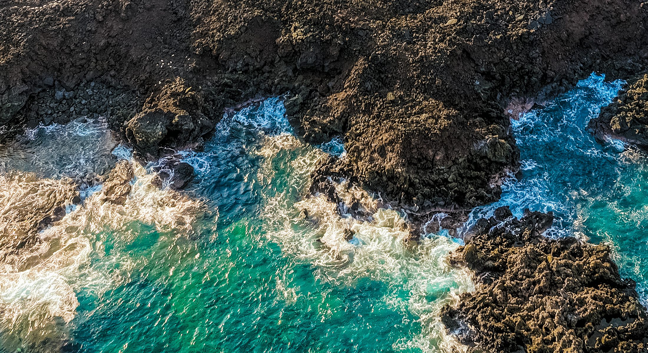 Turquoise surf breaking on black lava, from above
